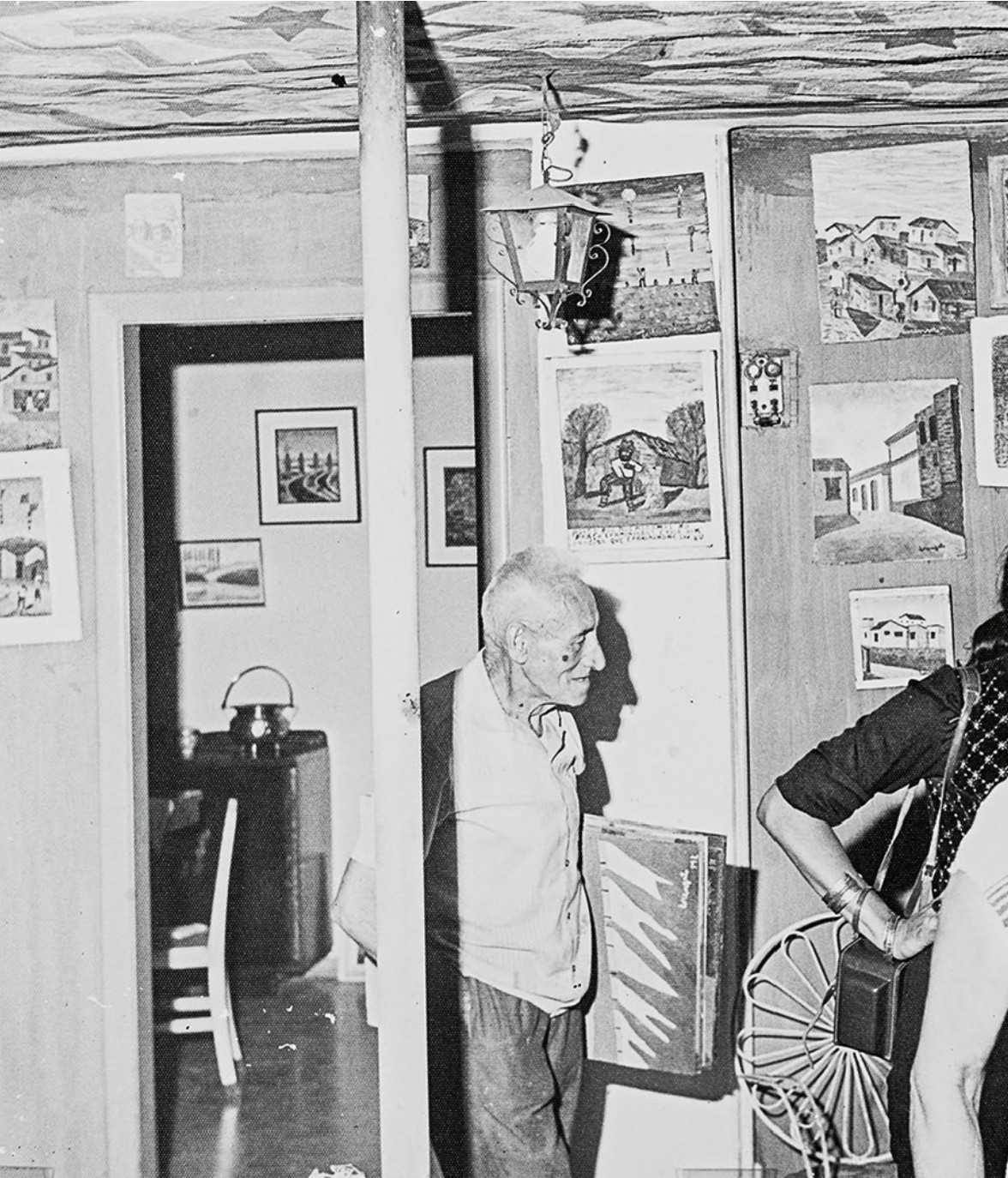 Fotografia em preto e branco de Lorenzato em seu ateliê, cercado de pinturas